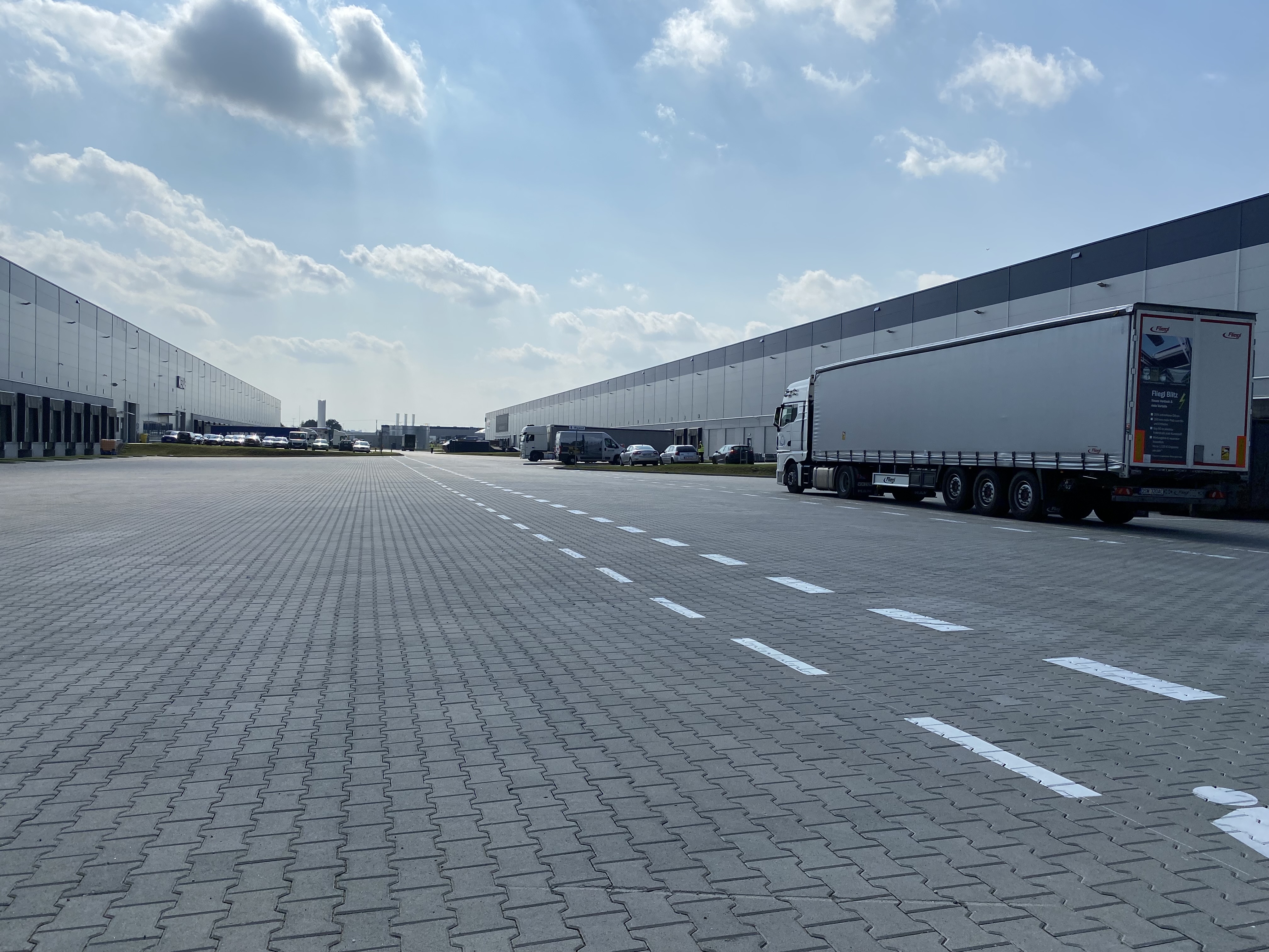 road showing warehouse on each side with a few trucks and cars