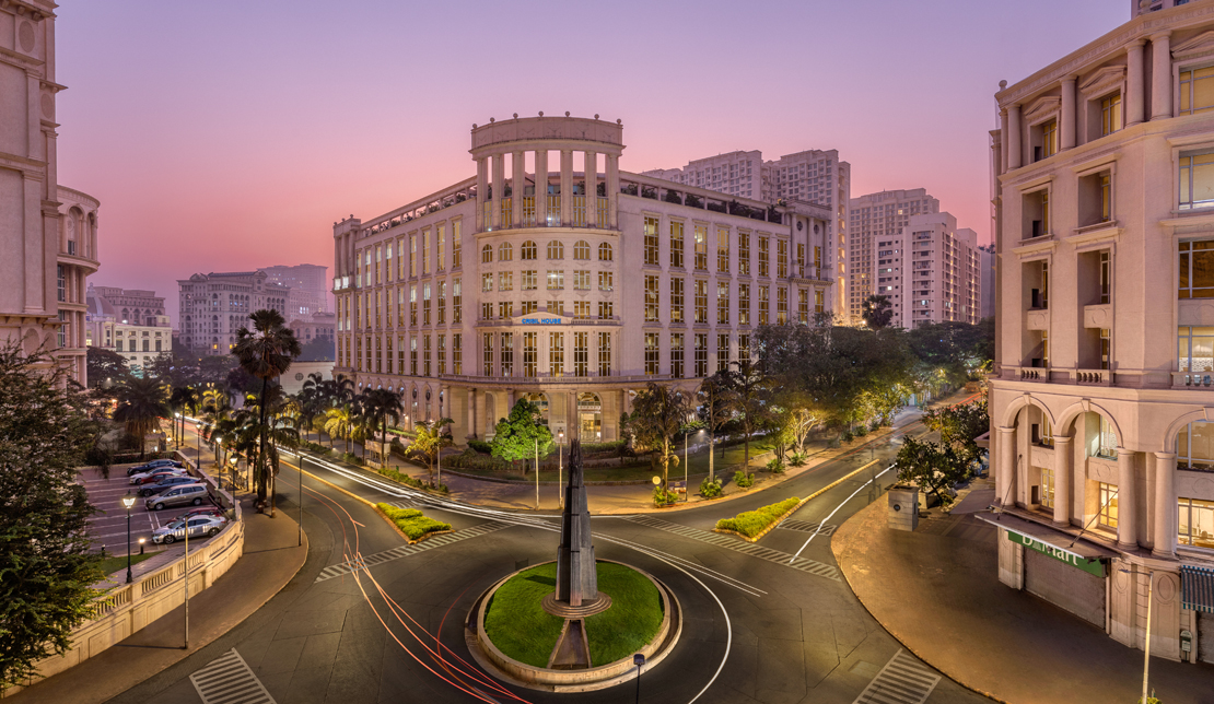 Downtown Powai at dusk and a traffic circle that is located near some buildings in the center of a town.