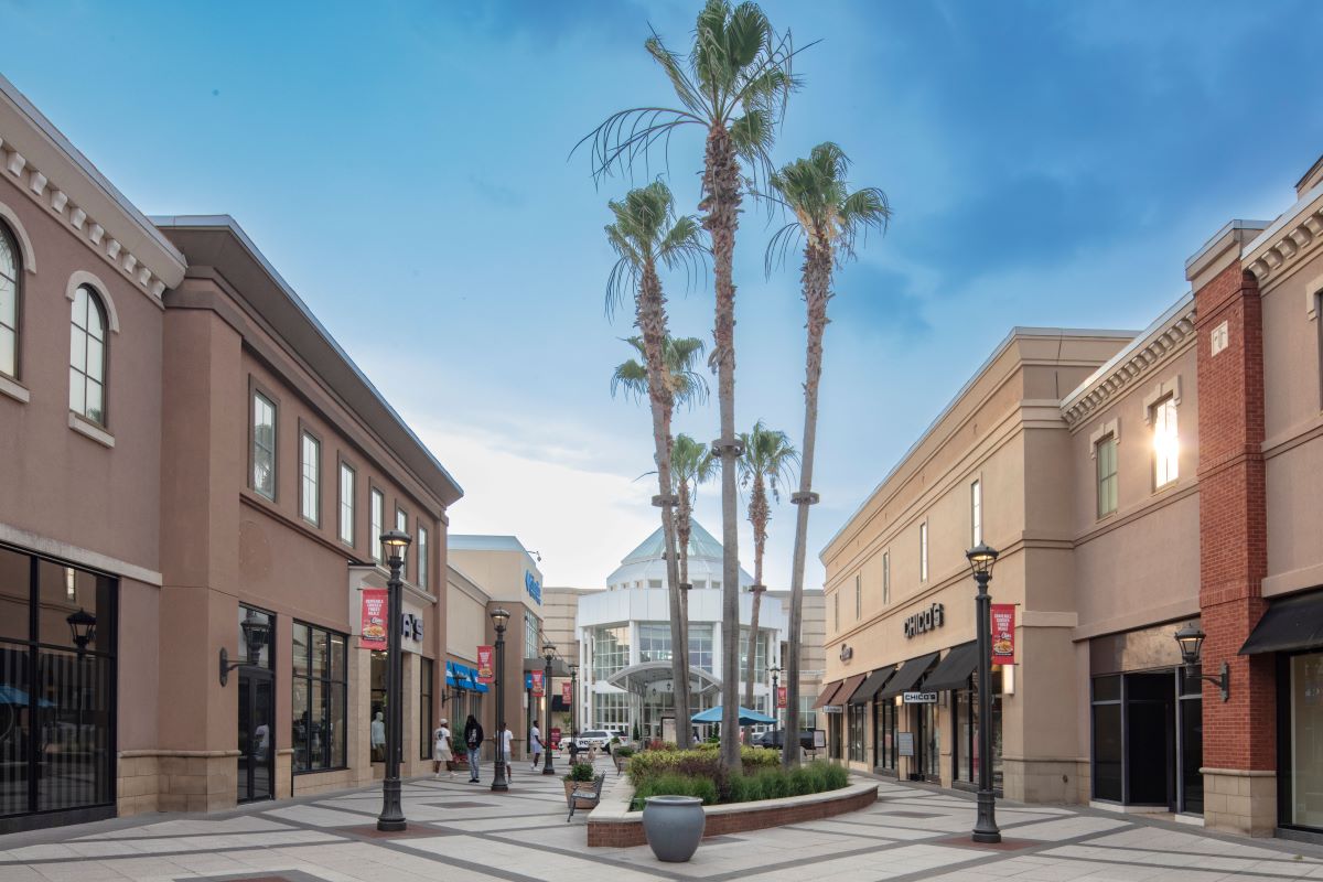 Outdoor photo of the shopping center showing several storefronts and palm trees
