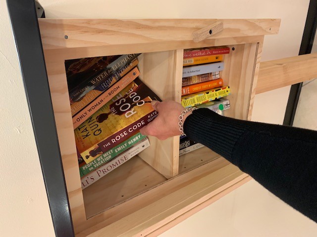 Hand pulling book out from Northbrook Court's Little Free Library